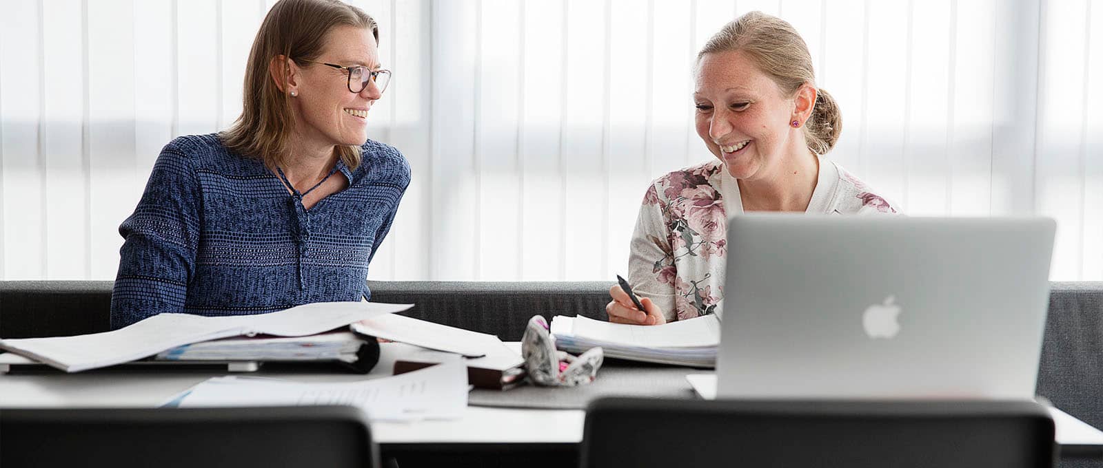 Två kvinnor ler mot varandra vid dator
